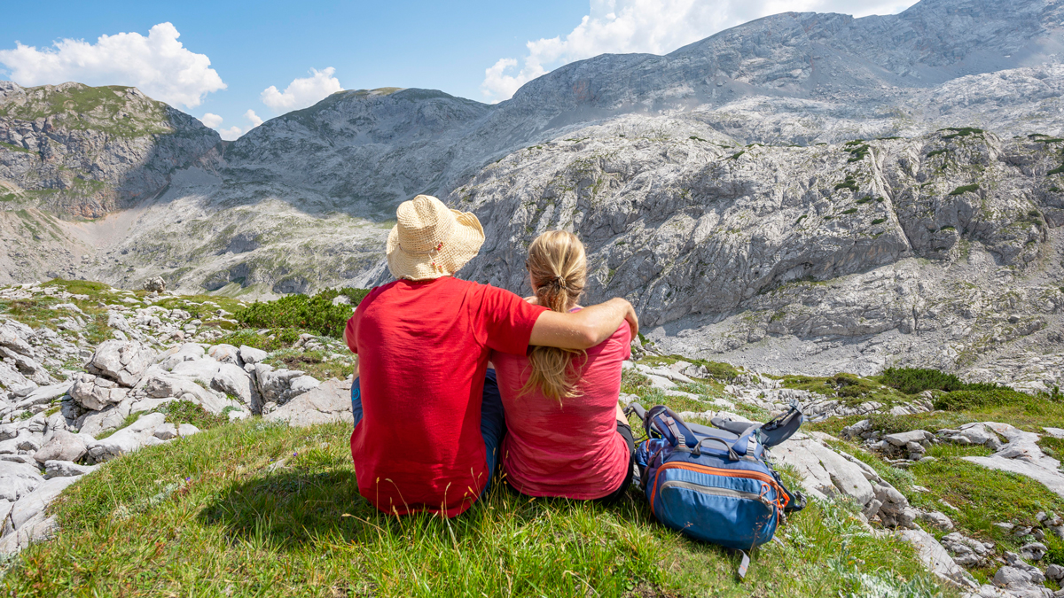 Мужчина с женщиной обнимаются, сидят на траве, смотрят на горы