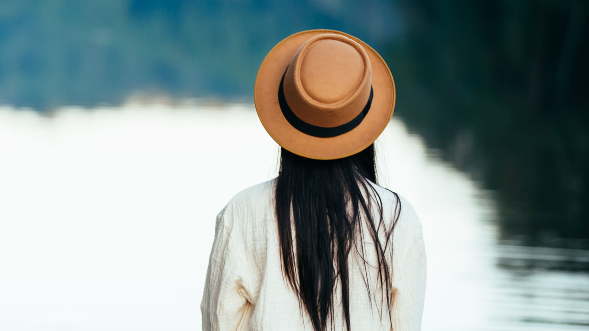 Одинокая девушка в шляпе на берегу озера